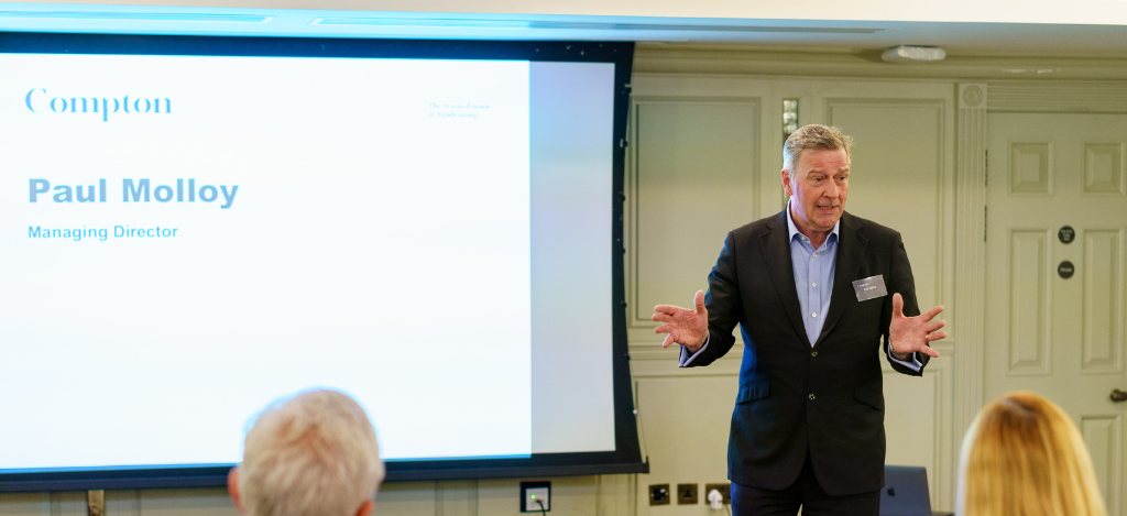 A white man in a suit delivering a presentation.